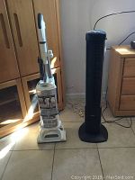 Shark upright vacuum and black Seville tower fan placed side by side on tile floor