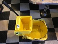 Yellow commercial mop bucket with attached wringer, showing black wringer handle and interior dirt marks.