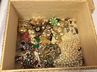 Overhead photo of lined box filled with over 15 shiny assorted costume jewelry pieces including necklaces, brooches, earrings, and bracelets.