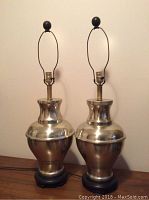 Pair of large vintage silver-colored metal table lamps with bulbous shaped bodies on carved wood bases, shown side by side.