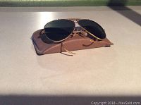Front view of Ray Ban gold rimmed aviator sunglasses resting on the original brown leather case.