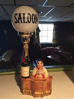 Full view of the ceramic saloon lamp showing the lamp base depicting a bartender behind a bar and the glass globe shade with 'SALOON' lettering.