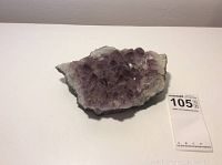 Large amethyst geode on a white surface with auction tag visible