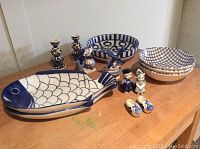 Overview of entire collection showing fish trays, patterned bowls, candlesticks, salt and pepper set, and figurines arranged on wooden surface.