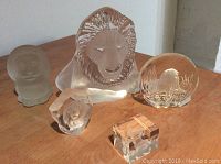 Full set of four crystal lion figurines on a wooden surface including frosted lion, lion head, lion in grass, and crystal cube.