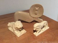 Three white lion figurines displayed on a wooden surface, showing different styles and sizes