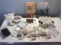 Full kit overview showing all items spread out on a white table, featuring beads in plastic packets, glass vials, reels of wire and thread, and the instructional book.
