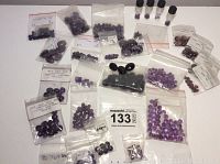 Amethyst cabochons and beads arranged on a flat surface, various sizes mostly in small ziplock bags and few vials.
