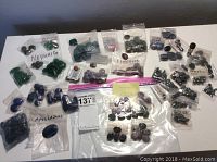 Various labeled plastic bags each containing polished cabochons and beads of different gemstone types arranged on a flat surface