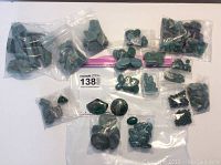 Wide view of multiple small plastic bags containing rough and polished malachite stones arranged on a white surface.
