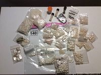 Overview of the entire lot showing numerous bags of pearl beads, cabochons, and mother of pearl pieces organized on a white surface.