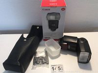 Canon 580EX Speedlite flash with box, soft carrying case, diffuser, mini stand, and lot tag on white table surface