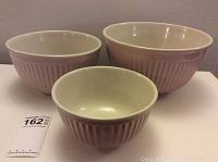 Set of three nested pale pink ribbed ceramic bowls shown on white surface.
