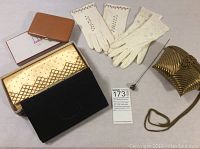Full view of the lot including two pairs of ladies gloves, three clutch handbags (black, gold-tone patterned, gold-tone ribbed with chain), an antique hat pin, and a Dunhill ostrich leather cigarette case in box.