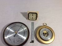 Barometers displayed side-by-side with measuring ruler for scale, shows varied sizes and styles.