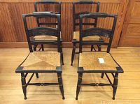 Front view of four Hitchcock chairs in black with rush seats, showing the set and general condition.