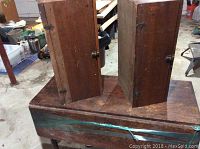 Two tall wooden storage boxes with hinged doors placed on top of a wooden table in a workshop setting.