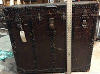 Front view of large vintage steamer trunk with metal rivets and corner protectors, showing overall condition and size using ruler.