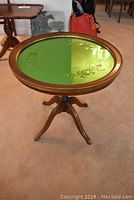 Full view of round table with green etched mirror top and three-legged wooden base.