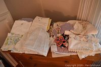 Overview of assorted white linens, folded pillow cases, crocheted doilies and embroidered placemats arranged on wooden dresser