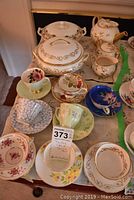 Image showing full tea set and covered bowls arranged on table, multiple cups and saucers with varied patterns and colors