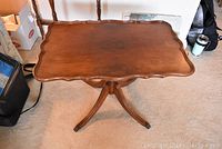 View of entire tilt-top table showing scalloped edge and four-legged base on carpeted floor