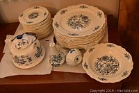 Wide view showing grouped dinner plates, side plates, bowl, salt and pepper shakers, and teapot with blue floral pattern on white china.