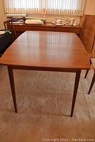 Full view of mid century modern wood dining table with tapered legs and finished wood surface