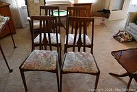 Four mid century dining chairs grouped closely showing floral upholstery on the seats and wooden frames with vertical slat backs.