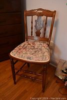 Front view of wood chair with floral seat cushion, showing turned legs and carved details on backrest.
