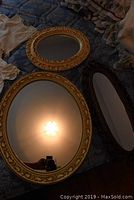 Three mirrors in the lot, one round with ornate gold ceramic frame and two rectangular with decorative plastic frames.