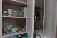 Two cupboards with kitchen items including floral china, glassware, plastic fruit, and Tupperware