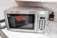 Front view of stainless steel Danby microwave, rectangular shape with a dark glass window and metal handle on the door.