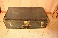 Full view of the black metal trimmed trunk placed on the floor showing overall condition and size.