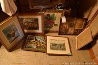 Eight framed art pieces arranged on floor including framed needlework rose print and animal paintings