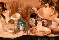 Full view of all items on table including ceramic pitcher and bowl with flowers, multiple decorative vases in various glass and ceramic styles, and mini plates with floral and cottage designs.