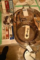 Overview of large silverplate serving platter with handles, a silverplate tray with decorative engraving, and multiple small travel spoons in original packaging and loose on the table.