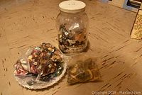 Large jar filled with various buttons and two plates/bags with more buttons on a wood floor.