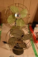 Two vintage Electrohome fans, one with green blades and one with silver blades, displayed on a table.