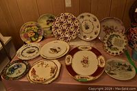 Image showing 11 porcelain decorative plates with varying floral, bird, and holiday scenes, some with gold trim.