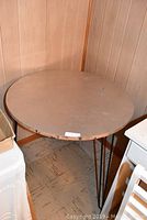 Round table seen from front corner showing metal top and three hairpin legs