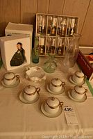 Photo showing boxed set of eight mid-century printed glasses, boxed Dave Grossman figurine, vintage glass bottles, cups and saucers, and candy dish on table