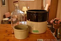 Wide shot of number 2 pickle crock, small butter crock, and large glass jug on wooden table