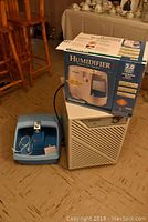 Three appliances shown together on floor: Duracraft humidifier in box on top of Simplicity dehumidifier. Blue foot bath to left.