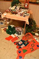 View of overall lot showing Christmas stockings, garlands, ornaments, decorative signs, and a red lantern-shaped light on a table and floor.