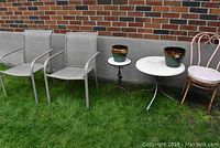Shows patio seating including two sling chairs, a round white metal table with two glazed clay planters on top and a pink metal ice cream parlour chair.