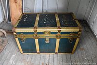 Front view of large metal clad trunk showing blue and yellow colors and brass latches and corners