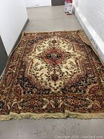 Full view of cream-base area rug with central medallion and border design laid flat on floor.