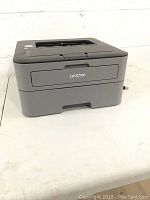 Front angle view of Brother laser printer showing front paper tray and top output slot.