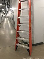 Photo of the full height of the orange fiberglass ladder with aluminum steps in an indoor hallway showing condition and details of construction.